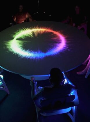 pessoas no escuro ao redor de um mesa com iluminação colorida