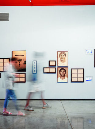 pessoas com imagem borrada passam em frente a obras da Exposição 37 Panorama MAM SP 2022