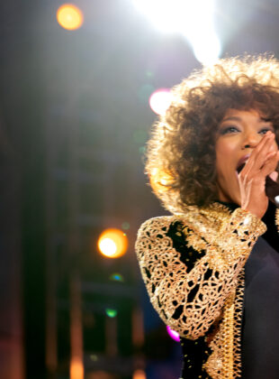 atriz naomi ackie caracterizada como whitney houston, com casaqueto preto com detalhes dourados