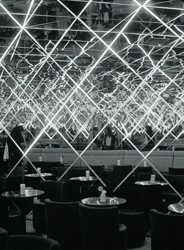 salão de bar em pb com luzes saindo das mesas e se cruzando em direção ao teto