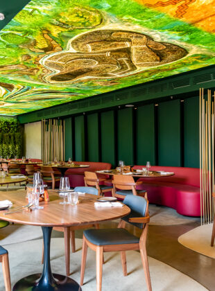 ambeinte de restaurante com mesas de madeira, sofás pink e teto decorado com pintura de floresta