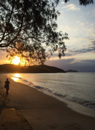 homem caminha na praia no por do sol