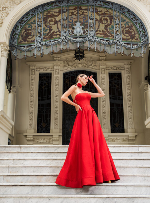 Modelo loira com cabelo preso em rabo de cavalo baixo usa vestido vermelho tomara que caia