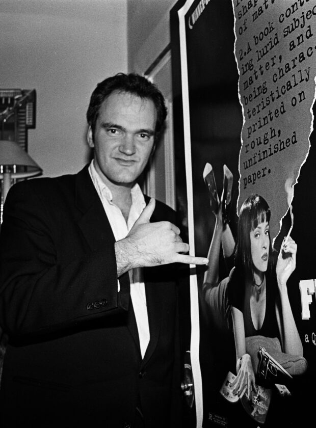 Quentin Tarantino ao lado do pôster de Pulp Fiction, em 1994