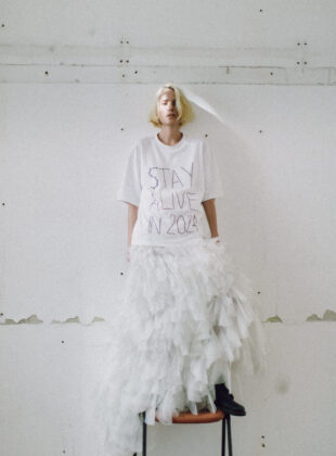 Modelo com camiseta branca onde se lê a frase Stay Alive in 2024 que faz parte da coleção de lançamento da Harpas, nova marca de Emannuelle Junqueira.